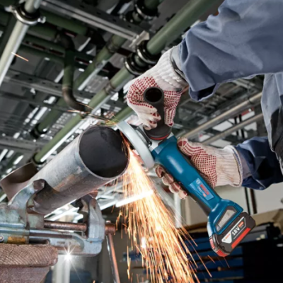 Pessoa a cortar tubo metálico com rebarbadora azul e preta em ambiente industrial