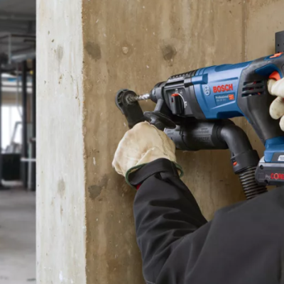 Pessoa usando ferramenta BOSCH azul e preta com luvas a trabalhar numa parede de cimento