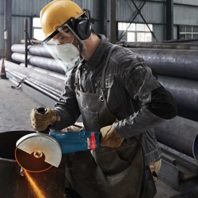 Homem a usar equipamento de proteção a cortar metal numa fábrica.