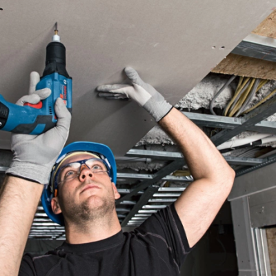 Homem a instalar painel de gesso com furadeira num teto de construção
