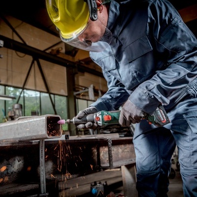 Homem com fato de trabalho azul e capacete amarelo a usar ferramenta elétrica numa oficina