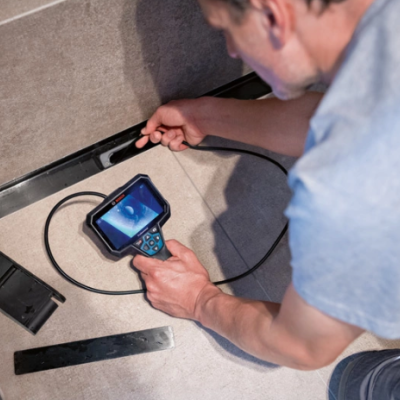 Homem usando câmera de inspeção portátil com cabo flexível em espaço com paredes cinzentas.