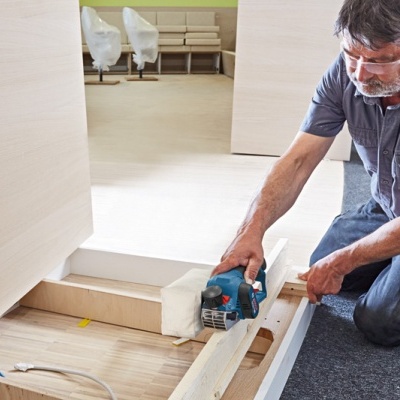 Homem com serra elétrica a cortar madeira clara em interior com decoração creme