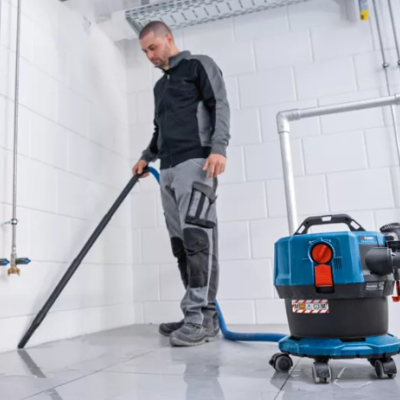 Aspirador industrial portátil azul e preto com tubo a ser usado por homem.