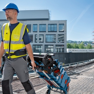 Trabalhador da construção com colete amarelo e capacete azul a puxar carrinho de ferramentas
