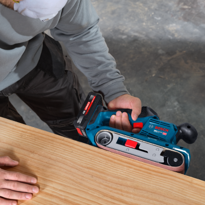 Lixadeira de fita BOSCH azul e preta em uso sobre madeira