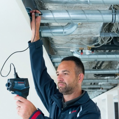 Homem a usar ferramenta elétrica Bosch para inspeccionar condutas metálicas no teto