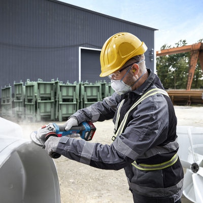 Homem com capacete e equipamento de proteção a usar ferramenta elétrica em estrutura metálica branca ao ar livre