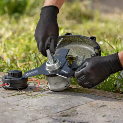 Mãos com luvas pretas a montar peça metálica numa máquina de corte sobre cimento