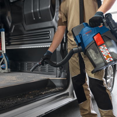 aspirador portátil BOSCH azul e cinza a ser usado para limpar dentro de uma carrinha