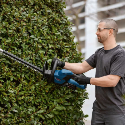 Homem a cortar sebe com tesoura eléctrica em ambiente exterior.