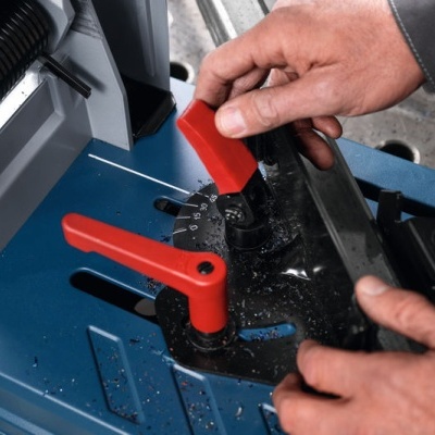 Máquina de corte azul com alavancas vermelhas e mão a ajustar peça metálica