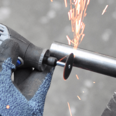 Mão com luva azul a usar ferramenta DREMEL para cortar tubo metálico com faíscas