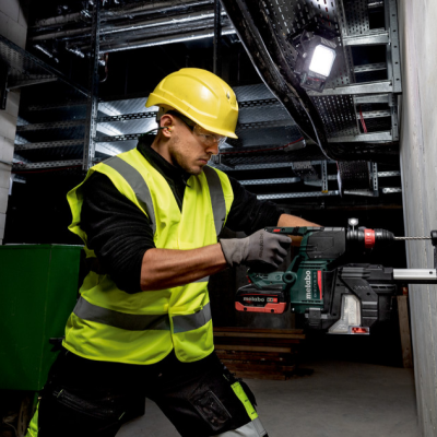 Homem com colete e capacete amarelo a perfurar parede com furadeira