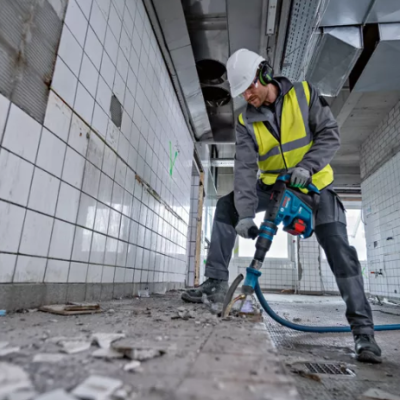 Trabalhador com martelo demolidor num espaço interior em construção com azulejos brancos
