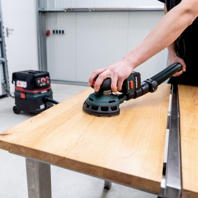 Lixadora elétrica preta e verde a ser usada em madeira numa oficina.