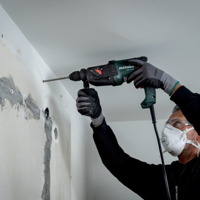 Pessoa a usar furadeira para fazer um furo numa parede branca com manchas de reboco cinza