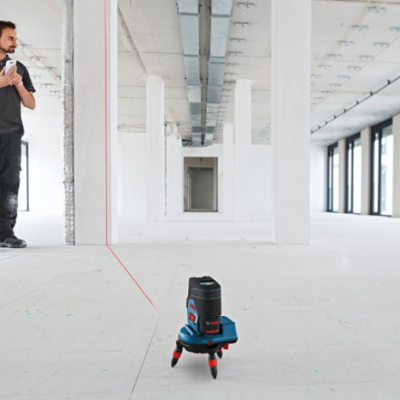Nível laser Bosch preto azul com linha vermelha no chão de espaço amplo vazio e homem ao fundo