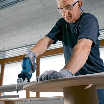 Homem a usar ferramenta elétrica Bosch azul para cortar tubo cinzento