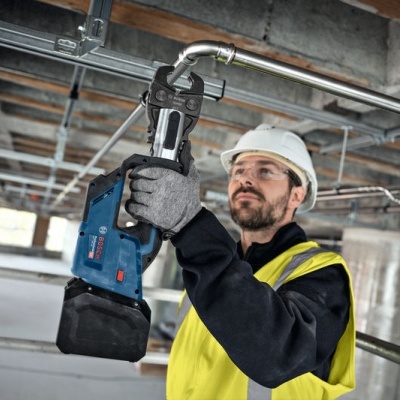 Homem com capacete e colete segurando ferramenta elétrica azul num ambiente de construção