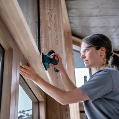 Mulher a lixar madeira com lixadora elétrica perto de janela