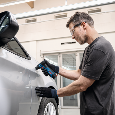Homem usando ferramenta elétrica numa lateral de carro branco