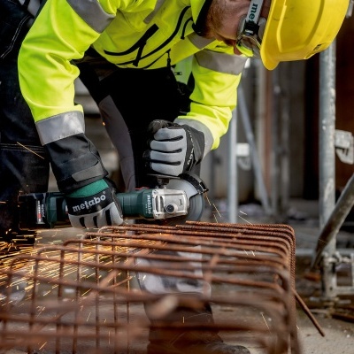 Trabalhador com capacete e rebarbadora a cortar ferro enferrujado numa obra