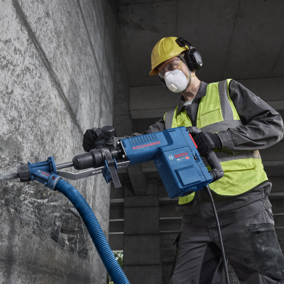 Martelo demolidor Bosch azul com mangueira de aspiração usado por trabalhador com equipamento de proteção na construção.