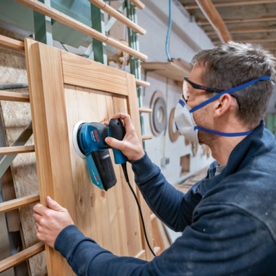 Pessoa a lixar porta de madeira clara numa oficina de carpintaria.