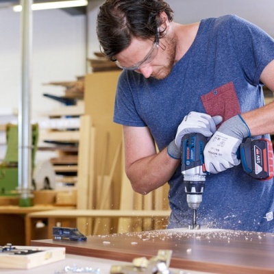 Homem a usar berbequim elétrica numa mesa de carpintaria