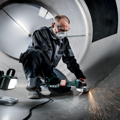 Pessoa a usar rebarbadora e máscara dentro de estrutura metálica cilíndrica