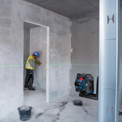 Divisão em construção com trabalhador, nível laser e baldes no chão