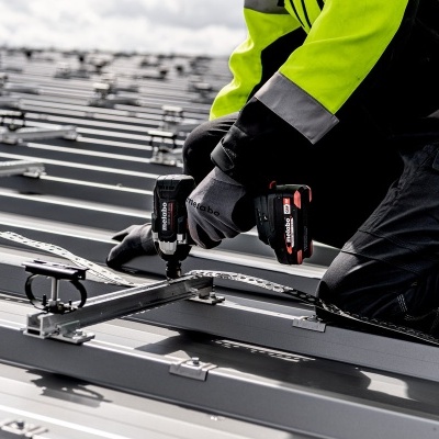 Trabalhador em roupa de alta visibilidade a montar estrutura metálica com ferramenta elétrica