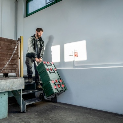 Homem a transportar caixa robusta verde com fechos vermelhos numa escada interior