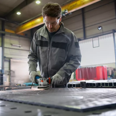 Homem a usar esmerilhadora vestido com roupa de trabalho cinzenta numa oficina industrial