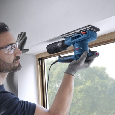 Homem a usar furadeira/parafusadeira Bosch azul perto de janela