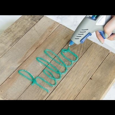 pistola de cola quente a escrever 'hello' em cola azul esverdeada sobre madeira