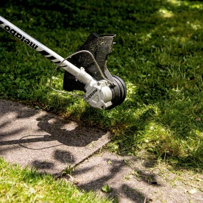 Aparelho de aparar relva metálico e branco em relva junto a caminho de pedras