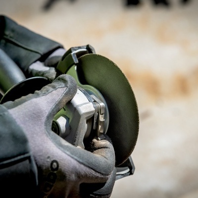 Pessoa a usar esmerilhadeira com disco abrasivo preto e luvas cinzentas