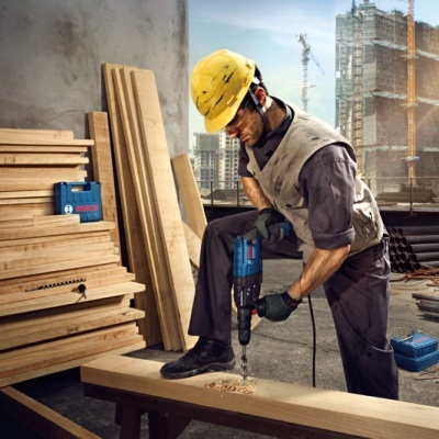 Homem a usar furadeira em tábua de madeira num canteiro de obras