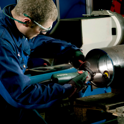 Pessoa a trabalhar em cilindro metálico com ferramenta elétrica numa oficina