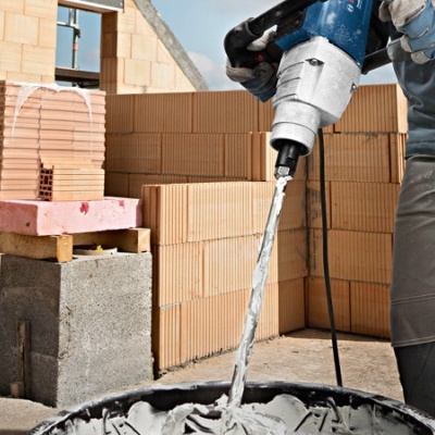 Trabalhador a misturar cimento com ferramenta elétrica num balde preto num canteiro de obras