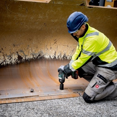 Pessoa apertando parafuso na lâmina de uma escavadora amarela