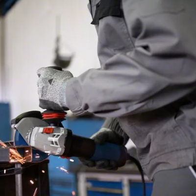 Pessoa com fato cinzento e luvas a usar esmerilhadora que emite faíscas numa oficina