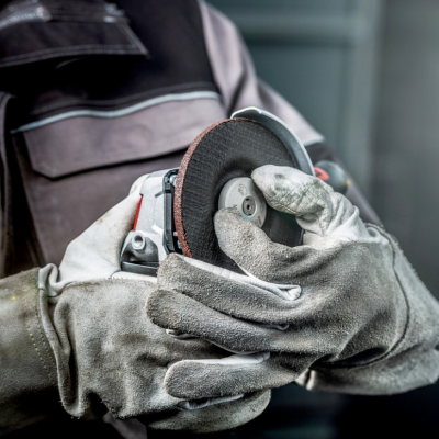 Pessoa com luvas segurando esmeril angular em ambiente industrial