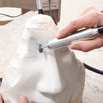 Escultura de rosto em pedra branca a ser trabalhada com ferramenta elétrica