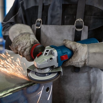 Pessoa a usar uma esmerilhadora elétrica azul numa chapa metálica com fagulhas