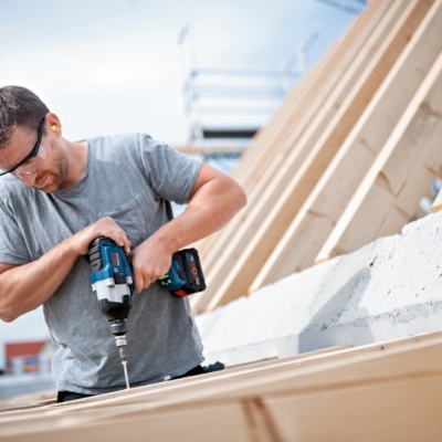 Homem a usar furadeira elétrica numa estrutura de madeira clara no exterior