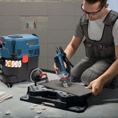 Máquina de cortar azulejos BOSCH azul e preto com colector de pó e homem a cortar azulejo cinza