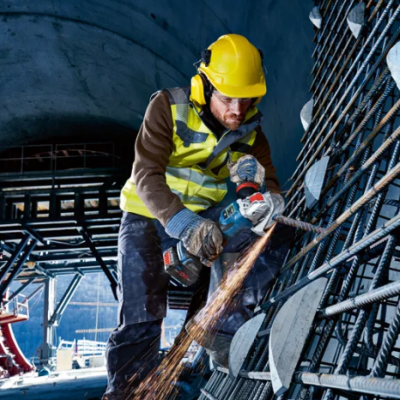 Trabalhador com capacete e colete refletor a cortar metal em obra dentro de túnel